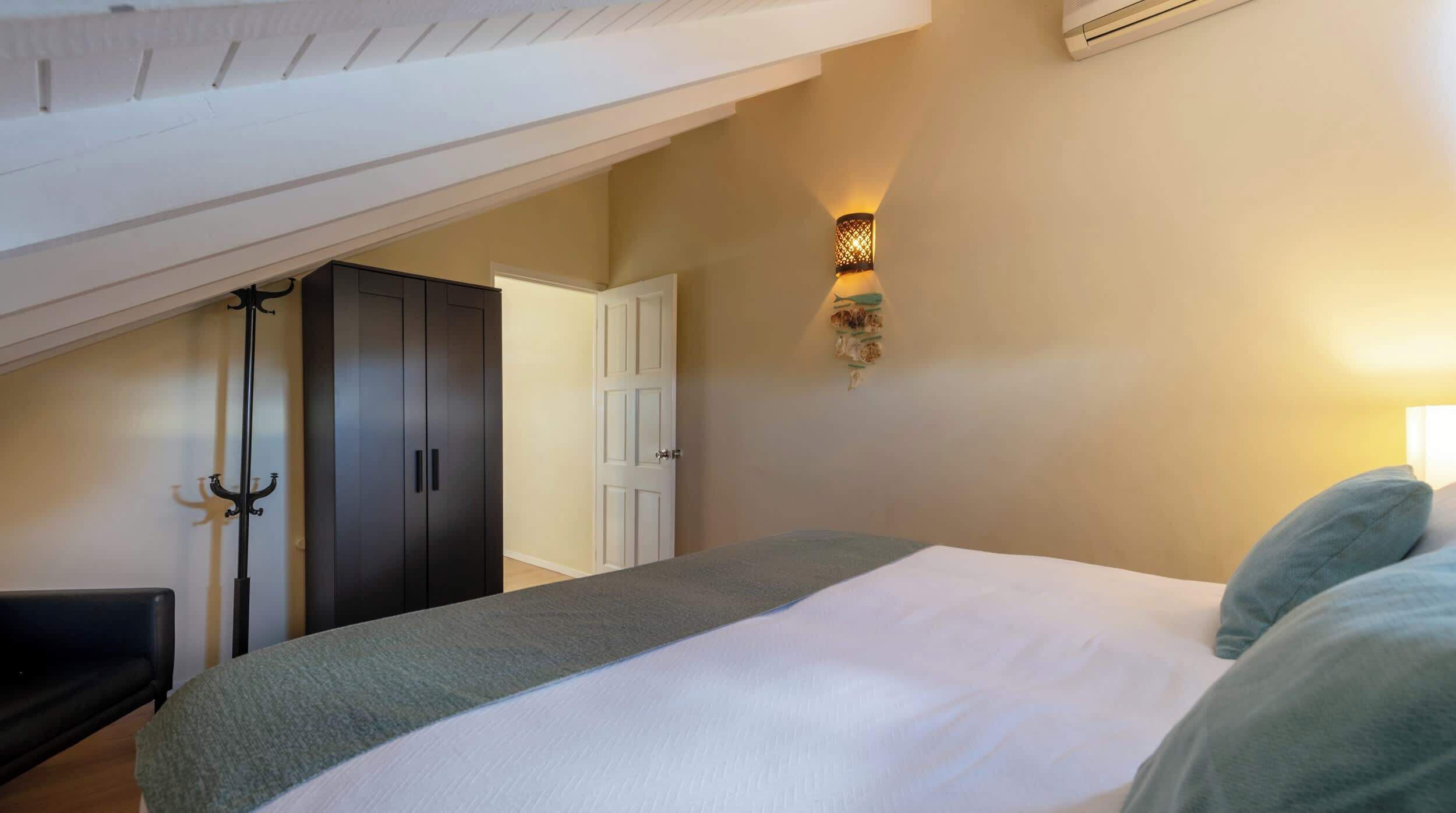 A bedroom with a bed, a coat rack, a wardrobe, and a wall-mounted light fixture.
