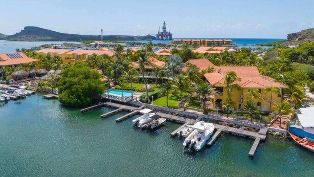 A coastal resort with a marina, palm trees, and a distant offshore oil platform. - Tropical Treasure |Sunset Penthouse Near Jan Thiel (Willemstad)