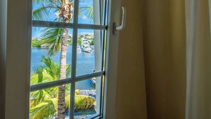 A window with a view of a marina, palm trees, and buildings across the water. - Tropical Treasure |Sunset Penthouse Near Jan Thiel (Willemstad)