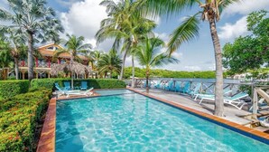 A swimming pool with clear blue water, surrounded by palm trees and lounge chairs. - Tropical Treasure |Sunset Penthouse Near Jan Thiel (Willemstad)