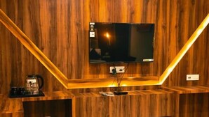 A room with a wooden wall, a flat-screen TV mounted above a wooden counter, and a chair in the foreground. - Hotel Sunshine Dharamshala (Dharamshala)