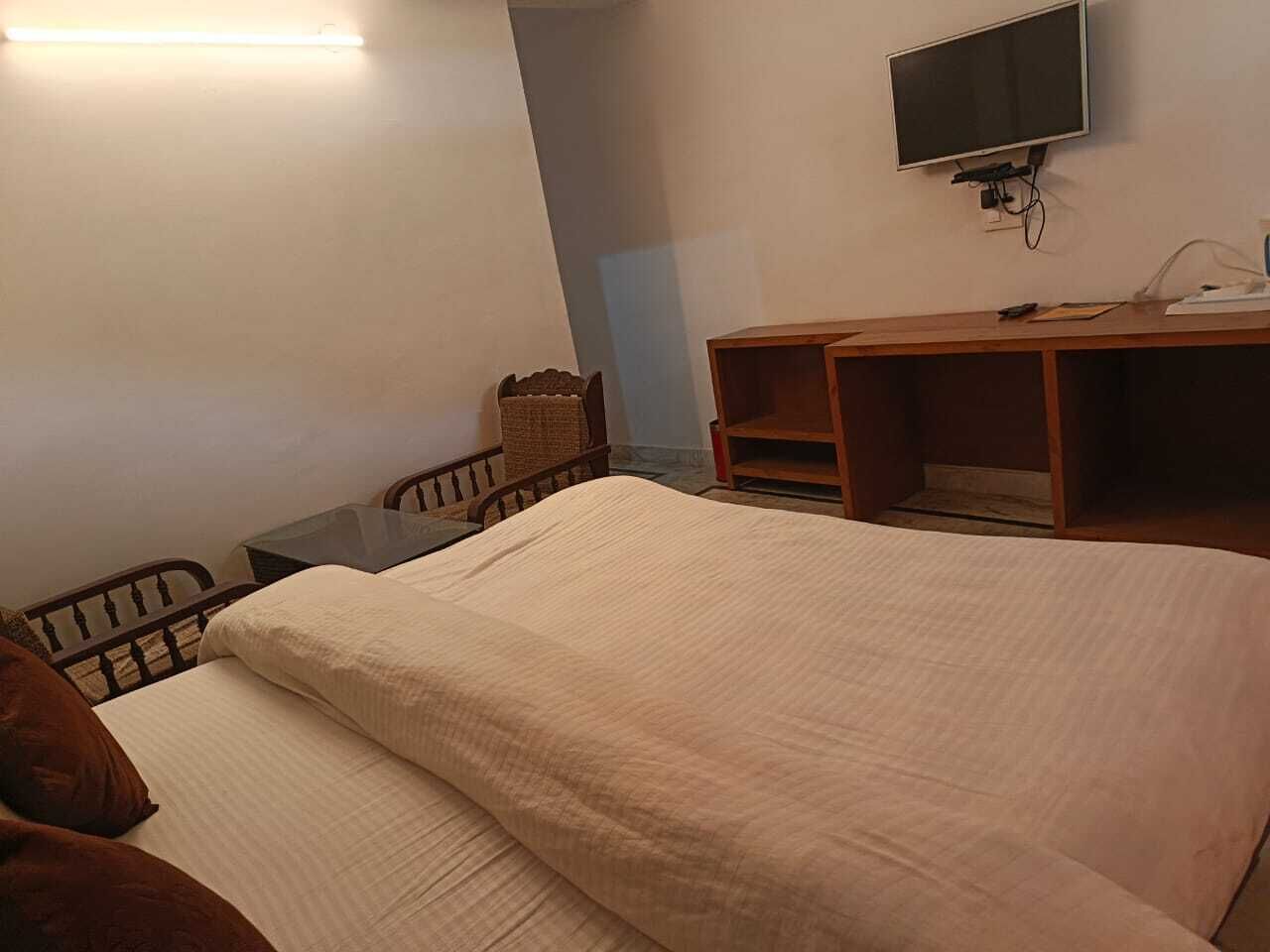 A bedroom with a bed, a desk, a chair, a television, and a wall-mounted shelf.