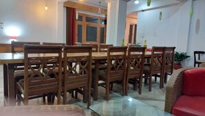 A dining area with wooden chairs and a glass table, a red sofa, and a wooden cabinet. - Hotel Sunshine Dharamshala (Dharamshala)