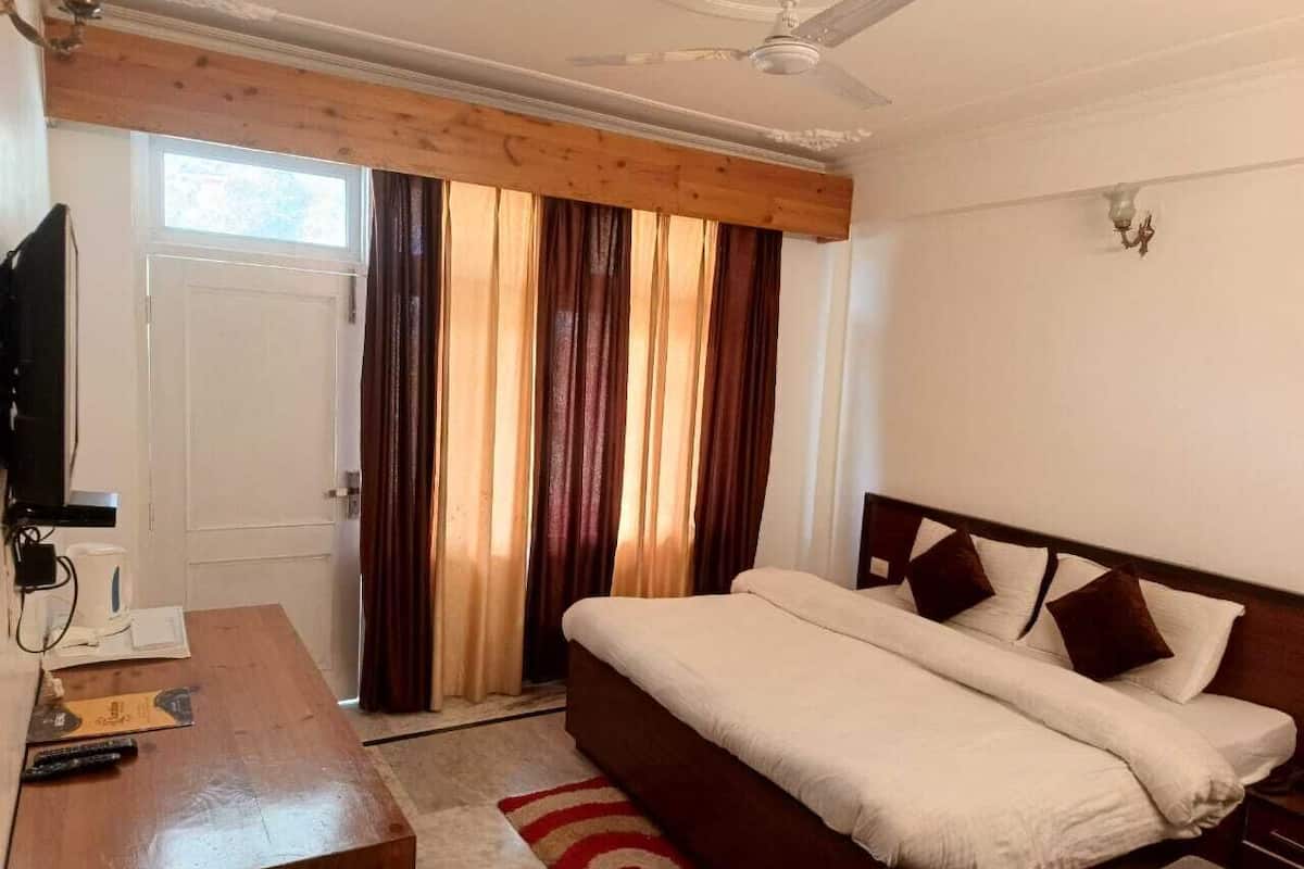Een slaapkamer met een bed, een houten bureau, een televisie en een raam met gordijnen.