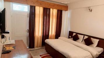 Un dormitorio con cama, un escritorio de madera, televisor y ventana con cortinas.