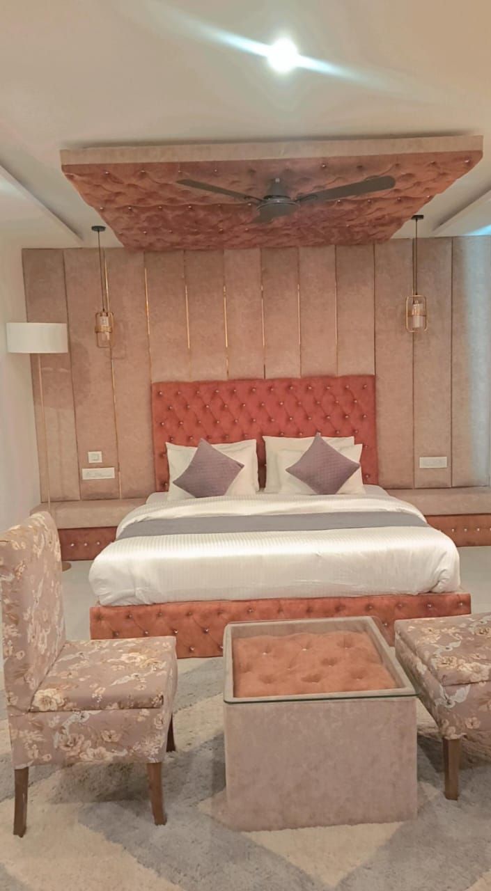 Une chambre à coucher avec un grand lit, deux fauteuils rembourrés, un petit pouf, un ventilateur de plafond et une lampe fixée au mur.