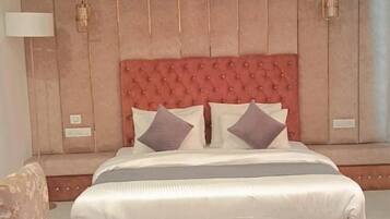 Une chambre à coucher avec un grand lit, deux fauteuils rembourrés, un petit pouf, un ventilateur de plafond et une lampe fixée au mur.