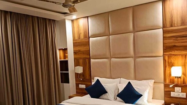 A hotel room with a large bed, a ceiling fan, wooden headboard, and a floral armchair. - Hotel Sunshine Dharamshala (Dharamshala)