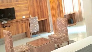 A modern hotel room with a bed, two armchairs, a coffee table, a flat-screen TV mounted on a wooden panel wall, and a ceiling fan. - Hotel Sunshine Dharamshala (Dharamshala)