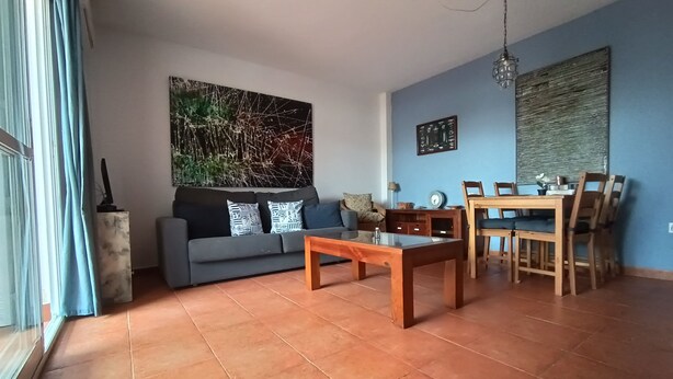 En stue med sofa, sofabord, spisebord og stole. Der er et maleri på væggen og et ur på væggen.