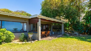 A modern house with a covered patio, large windows, and a well-maintained lawn. - Hilltop Hideaway (eMdloti)
