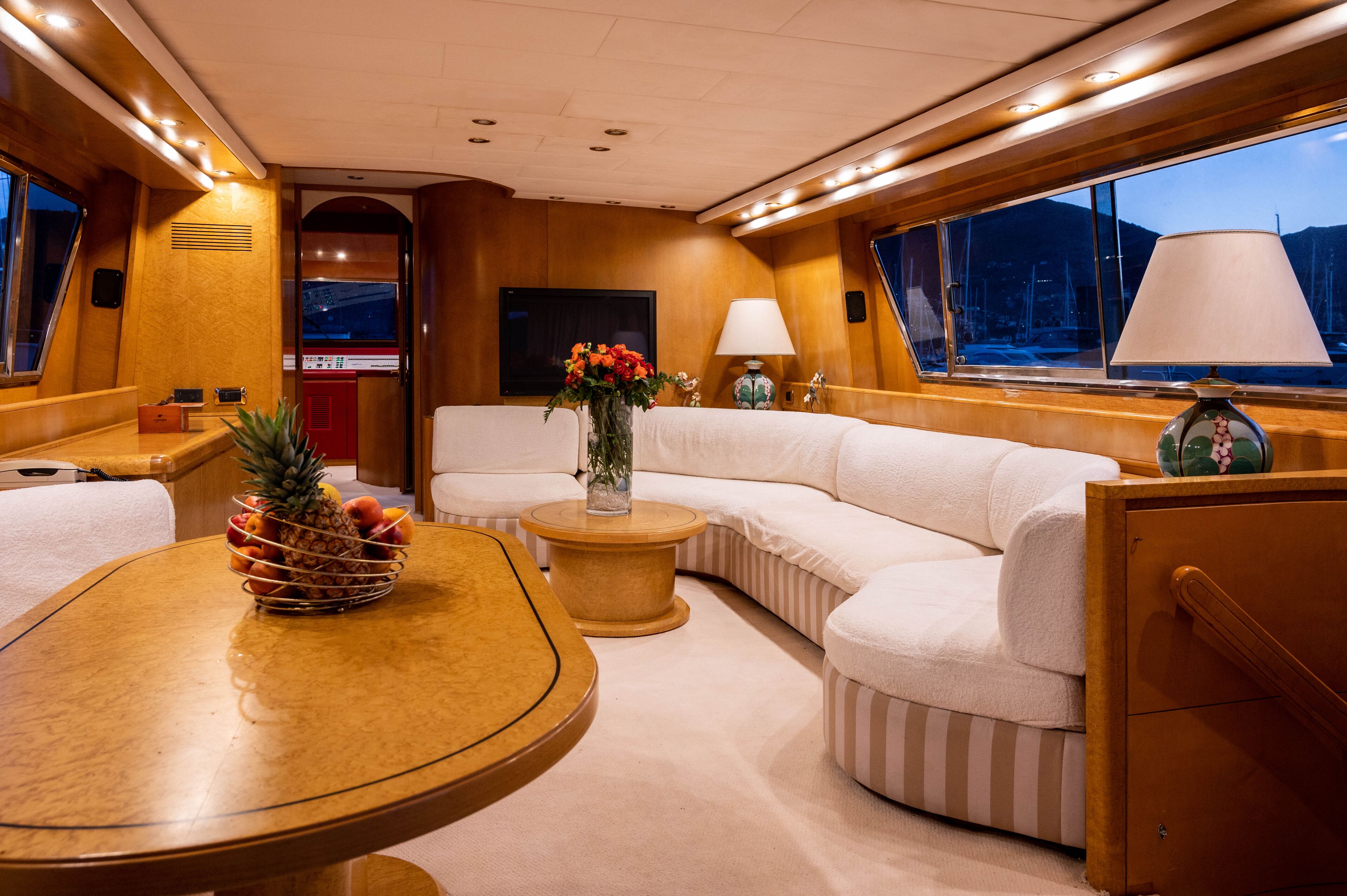 A yacht interior with a round dining table, a sofa, a small side table, and a large window with a view of the sea.
