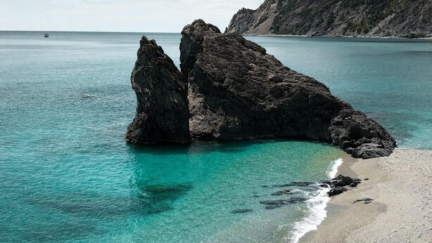 Een kustlandschap met helder turquoise water, een rotsachtige richel en een kiezelstrand.