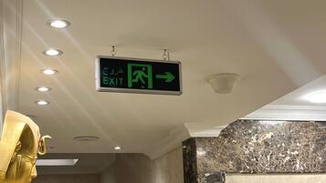 A hotel corridor with an exit sign, recessed lighting, a marble wall, and a gold-colored sculpture.