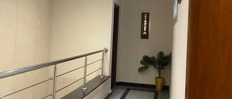 Un pasillo moderno con barandilla de vidrio, una planta en maceta y un cartel en la pared.