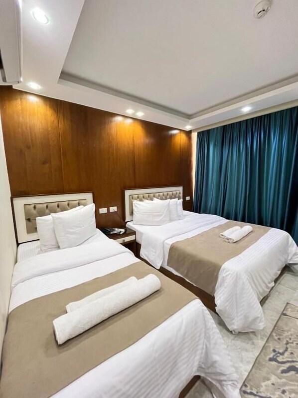 Habitación de hotel con dos camas, paneles de madera en las paredes, una cortina azul y una alfombra estampada.