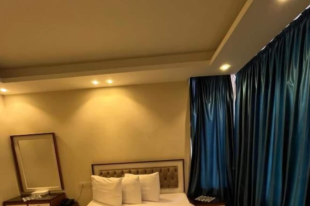 A hotel room with a large bed, two bedside tables, a mirror, and a curtain.
