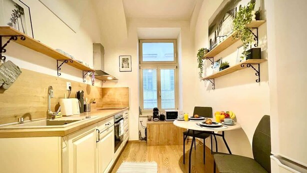A compact kitchen with wooden cabinets, a dining area with a table and chairs, and a window providing natural light. - Elegant Apartment on Hlavná Košice (Košický kraj)