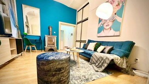 A modern living room with a blue accent wall, a round ottoman, a blue sofa, and a round coffee table. - Elegant Apartment on Hlavná Košice (Košický kraj)