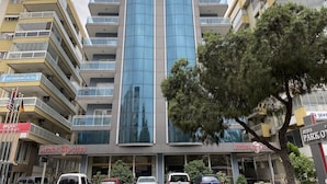 A multi-story hotel with a prominent central glass facade, balconies on each floor, and a flag on the left side. - Aydın Park Otel (Aydin)