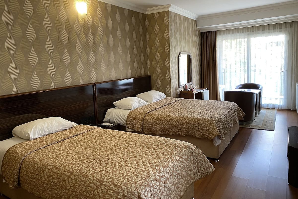Hotelkamer met twee bedden, een bureau, een stoel, een spiegel en een raam met gordijnen.