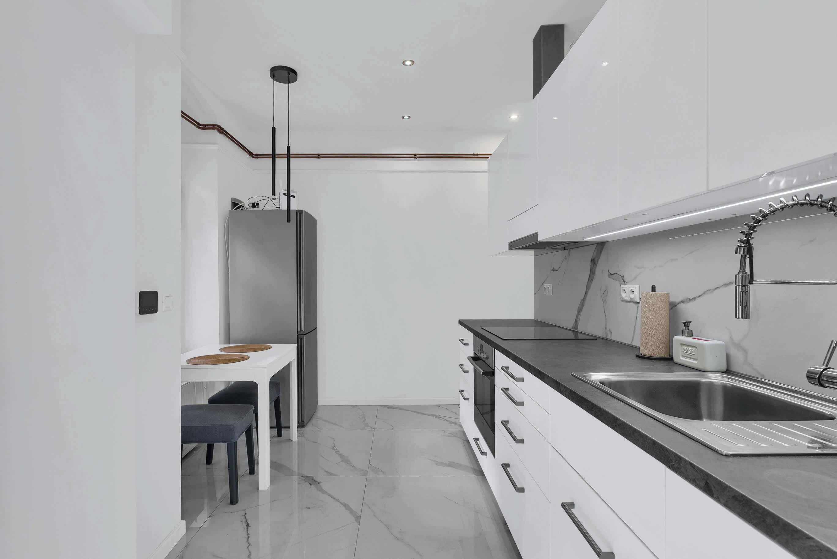 A modern kitchen with white cabinets, a stainless steel sink, and a marble countertop.