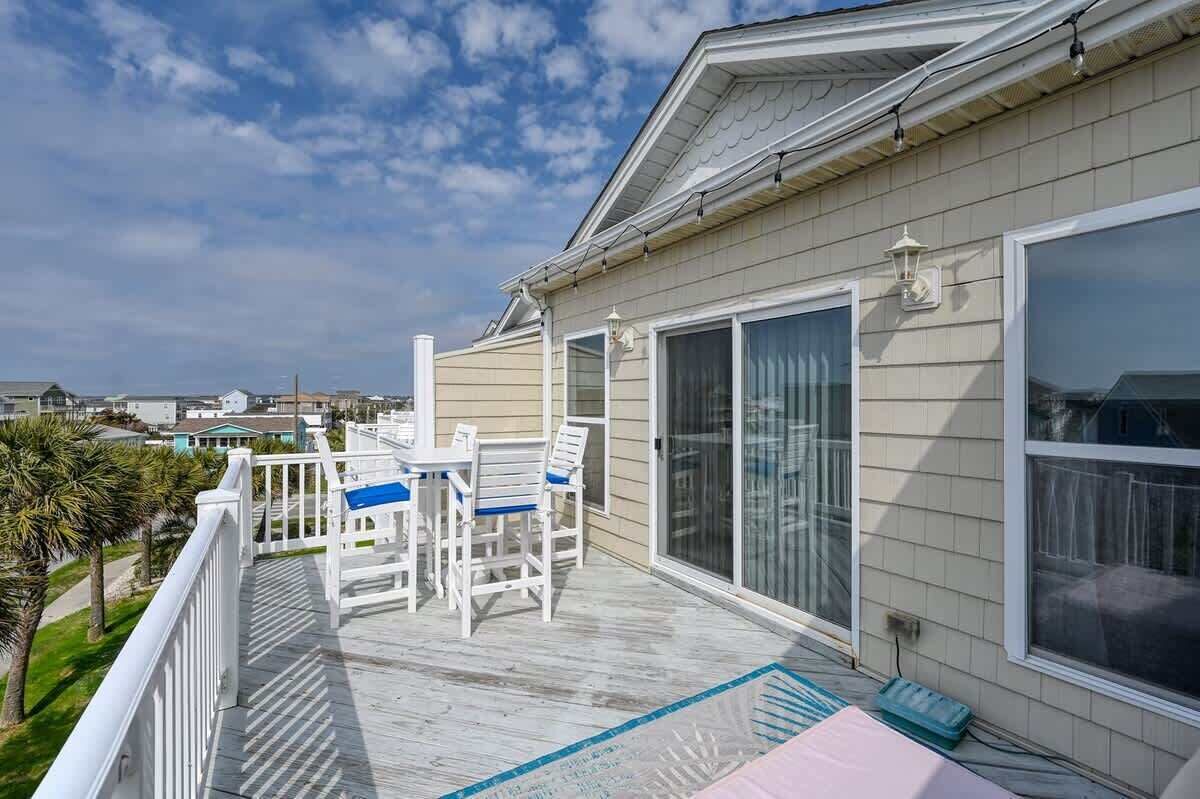Ein Balkon mit Meerblick, eine überdachte Terrasse mit Stühlen und eine große Schiebeglastür.