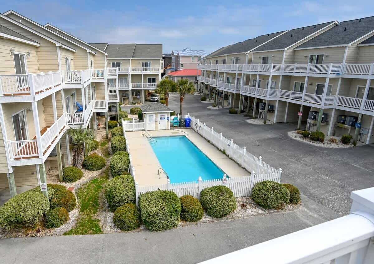 A motel with a central swimming pool, multiple balconies, and a fenced parking area.