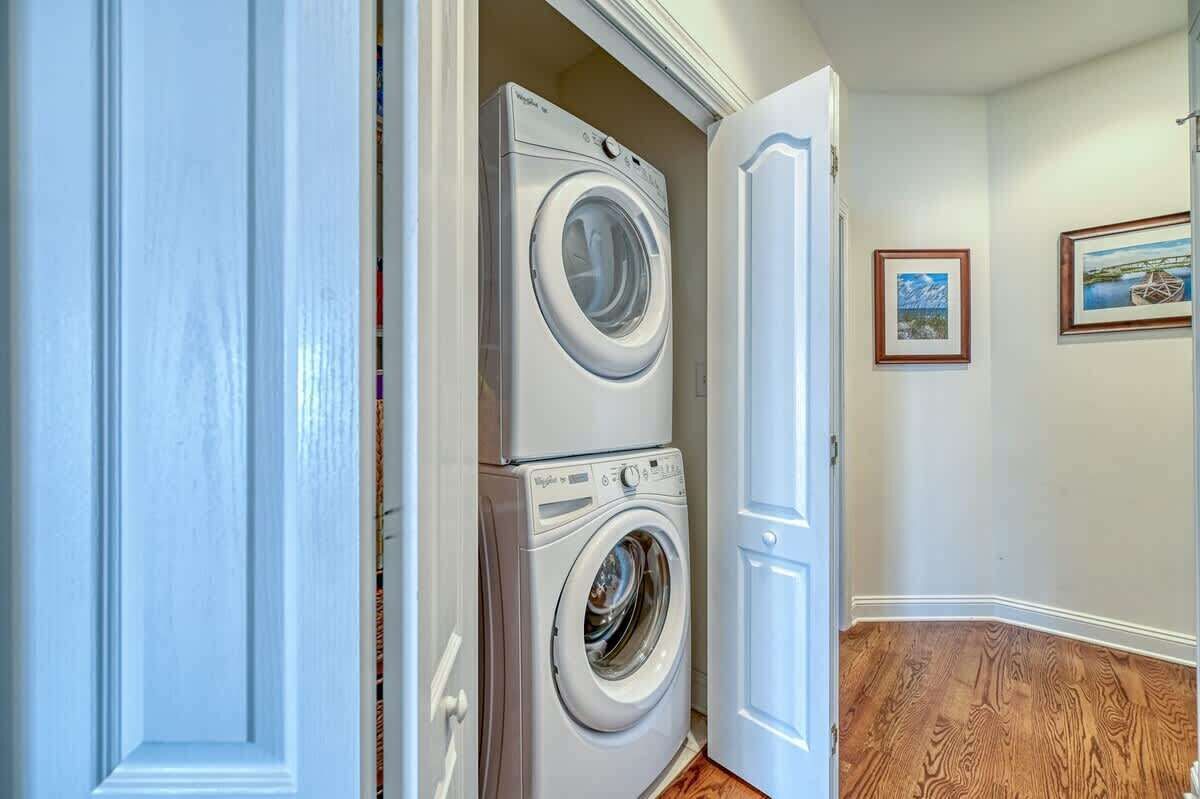 A laundry room with two stacked front-loading washing machines, wooden flooring, and framed artwork on the walls.