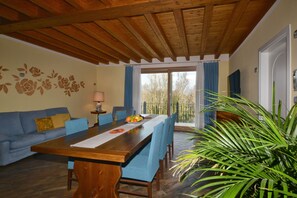 Ein Essbereich mit einem Holztisch, blauen Stühlen, einer Couch und einem großen Fenster mit Vorhängen.