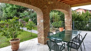 Un patio exterior con un arco de ladrillo, una mesa de vidrio y sillas.