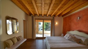 Un dormitorio con una cama grande, vigas de madera en el techo, un banco y un ventanal corredero que da a un espacio al aire libre.