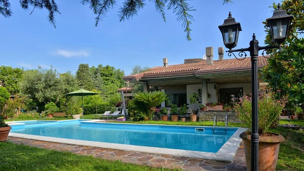 Una piscina con borde de piedra, rodeada de césped cuidado y plantas en macetas.