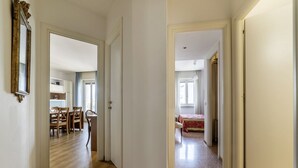 A hallway with wooden flooring, a dining area with chairs and a table, and a bedroom with a bed and curtains. - GuestHost - Cozy apartment of 90 sqm, can accommodate up to 5 people, located on the sixth floor of a building with a lift (NOT suitable for disabled people).The property is located in an area well connected by public transport, the metro line B Piramid (Roma)