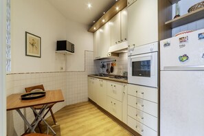A compact kitchen with white cabinets, a wooden table, a stove, and a refrigerator.