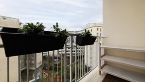 A balcony with black planters containing green plants, a view of a courtyard with buildings, and a white railing. - GuestHost - Cozy apartment of 90 sqm, can accommodate up to 5 people, located on the sixth floor of a building with a lift (NOT suitable for disabled people).The property is located in an area well connected by public transport, the metro line B Piramid (Roma)
