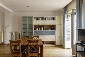 A modern kitchen with built-in cabinets, a dining table with chairs, and a television on a stand.