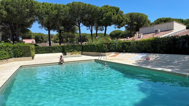 A rectangular swimming pool with clear blue water, surrounded by a tiled deck and lush greenery. - Chalet in a shady residence with swimming pool (Occitanie)