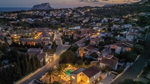 An aerial view of a coastal town at dusk with houses, a prominent mountain in the background, and a street leading to a building with a pool. - Large Villa with sea view in delightful Benissa Montemar (Costa Blanca North) (Benissa)