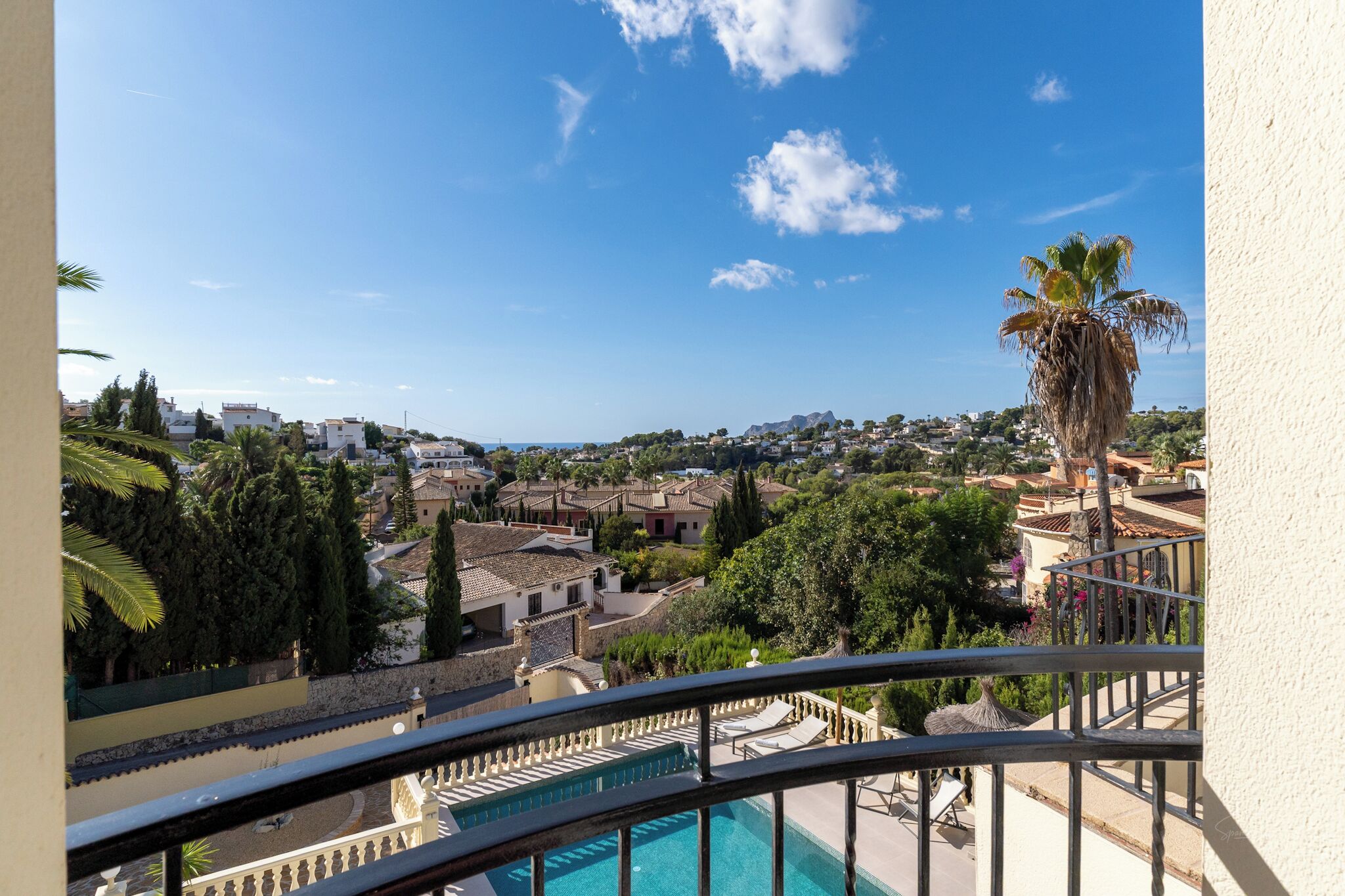 A balcony with a pool, overlooking a town with buildings and palm trees.