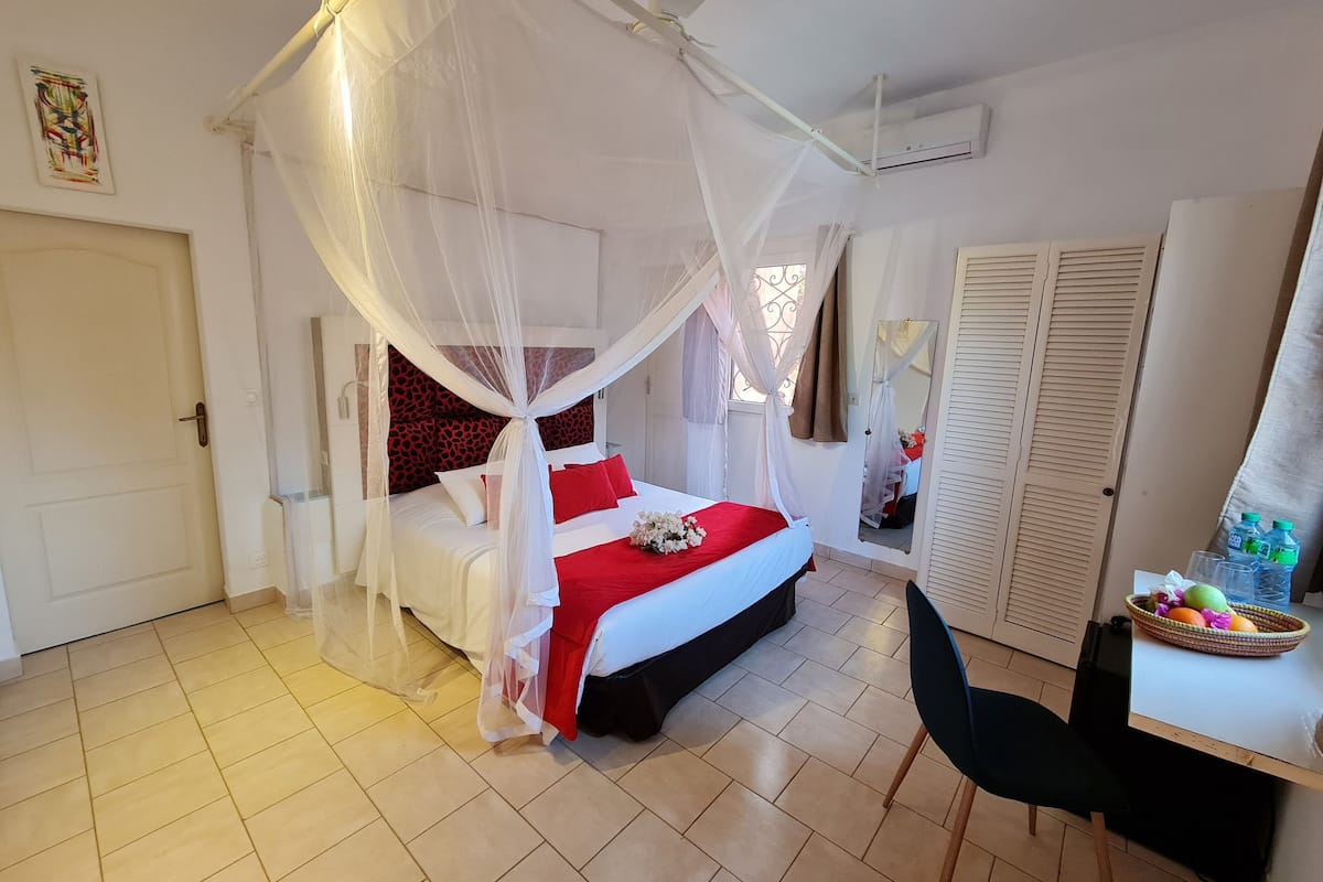 Een slaapkamer met een bed onder een baldakijn, een bureau met een stoel en een garderobe.