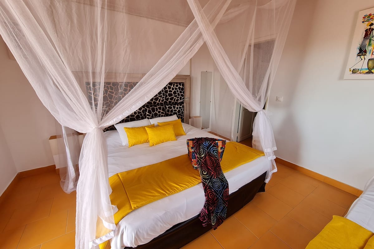 Een bed met hemelbed, witte beddengoed en gele accenten.