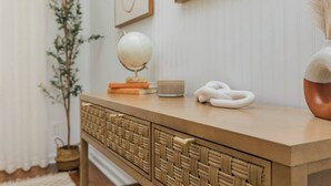 A wooden console table with a woven front panel, a globe, books, a candle, and a vase with dried plants. - Private Pool Oasis | 4BR Near Downtown Perry (Perry)