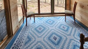 Ein Blockhaus-Interieur mit Holzboden, einem blauen Teppich mit Muster und einem großen Fenster mit Blick auf einen Wald.