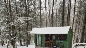 Eine Hütte in einem verschneiten Wald, im Vordergrund ein Hund.