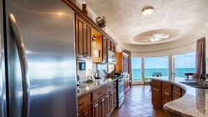 Una cocina con un refrigerador grande, armarios de madera, un microondas y vista al océano.