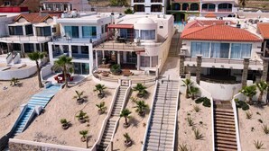 Un resort con varias edificaciones, piscina y una zona de arena con palmeras.