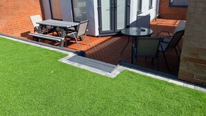 Un'area patio con struttura in vetro, un tavolo, sedie e un prato.