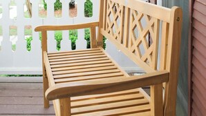 Un banc en bois sur un porche, avec une clôture blanche en bois et des plantes vertes en arrière-plan.