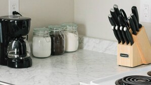 Une cuisine avec des meubles blancs, une machine à café, des bocaux d’épices et un bloc à couteaux.